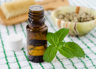 Small bottle with essential mint oil and fresh spearmint green leaves. Aromatherapy and herbal...