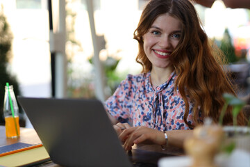 Young woman in a cafe, working on a laptop, embodies modern freelance success with a cheerful smile.