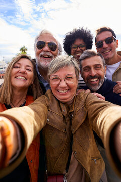 Cheerful vertical selfie of a group of mature people looking at camera happily, taking photos during their family trip together.