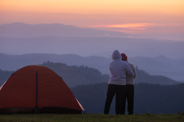 Couple is hugging each other by the tent during overnight camping while looking at the beautiful...