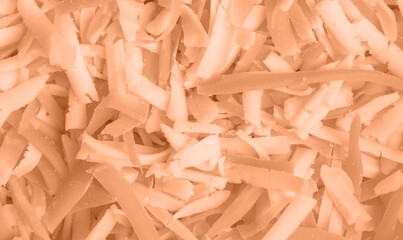 The background of grated cheese colored in new trendy color of 2024 year Peach Fuzz. Monochrome. Abstract. Wallpaper for blogs in social networks. Copy space