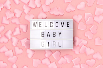 Welcome baby girl. Lightbox with letters and confetti in a heart shape on a pink background.