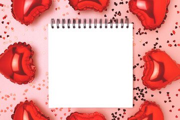 Frame made of red inflatable foil balloons in a heart shape. Blank notepad mockup on a pink...