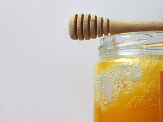 Crystallized honey in the glass jar on the gray background. Half of the honey jar, with wooden spoon and text area. 