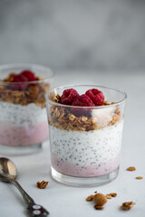 Raspberry chia seed parfait made with granola and berries in a cups with peony flowers on the background.