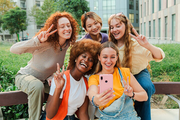 Happy multiracial young women looking at camera with a modern smart phone enjoying together sitting...