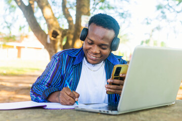 excited African student on headphone using cell phone and book for school work