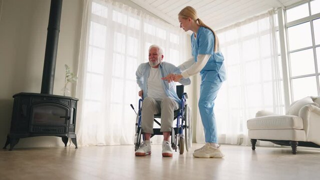 Nurse helps old wheelchair man to drink. Physical therapist woman provides medical help support to senior paralyzed male giving water. Palliative care in late stage of neurodegenerative pathologies.