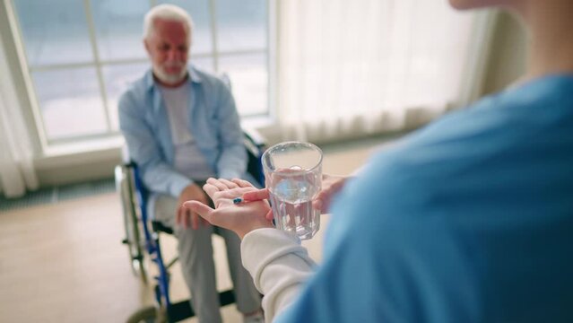 Nurse gives old wheelchair man pills. Physical therapist woman provides medical help support to senior paralyzed male gives water medications. Palliative care of neurodegenerative pathologies concept.