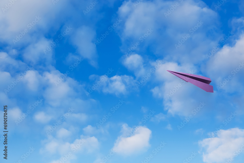 Wall mural Purple paper plane flying in blue sky with clouds