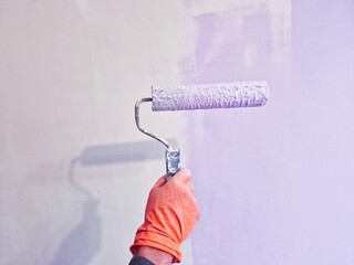 Close up of an artist's hand in a orange glove painting a wall with a paint roller, copy space.