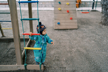 Little girl stands near a rope ladder and looks away