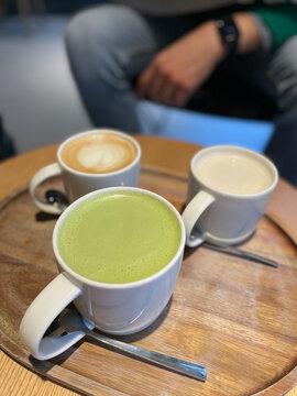Tres lattes diferentes sobre una mesa redonda de madera con un hombre desenfocado de fondo