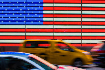 Moving yellow taxi and other cars passing US neon Flag