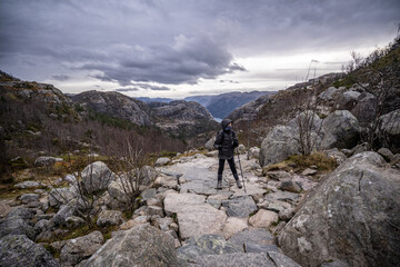 Hiker girl with trekking sticks and backpack walking on rocky terrain in the mountains , back view