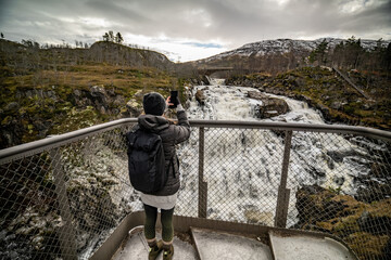 woman with backpack taking photo of Vøringfossen waterfall with no face