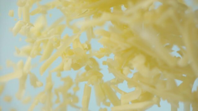 Heap grated cheddar cheese flying in slow motion close up. Shredded yellow parmesan cheese falling in macro. Ungraded raw ProRes footage for grading