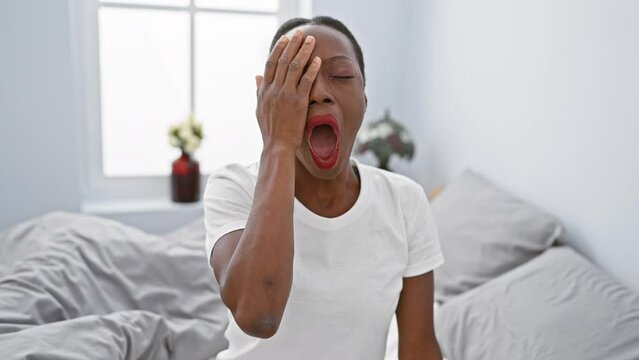 Exhausted african american woman in bedroom, fatigue covering half her face, hand on mouth, yawning tiredly