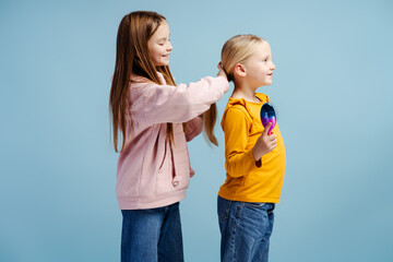 Cute beautiful girl brushing her little sister's hair, doing her hairstyle, wearing colorful clothe