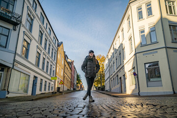 young pretty woman on the pavement of the town of alesund with tradidional houses on background - obrazy, fototapety, plakaty