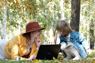Mother and daughter are studying in the park using a laptop. Training, game education