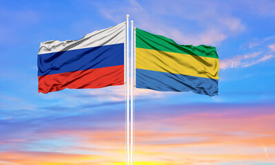 Russia and Gabon two flags on flagpoles and blue sky.