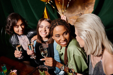 overjoyed and elegant multiracial women holding champagne glasses during birthday party in bar