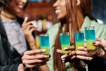 cropped view of blurred multiracial girlfriends holding shot glasses in modern bar, hen party