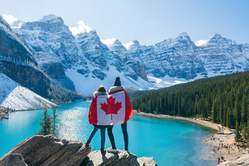 Tourists draped in Canadian flag looking beautiful scenery of Moraine lake. Banff National Park. Canadian Rockies. Alberta, Canada.