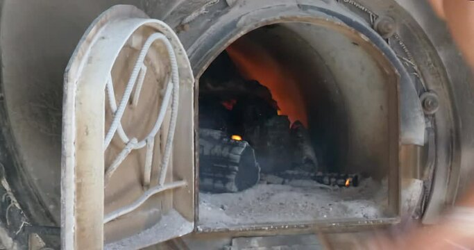 close-up of the worker adds wood to feed a fire inside a kiln 