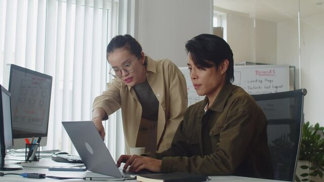 Medium long slowmo of female tutor guiding new male coder and helping with application developing using laptop