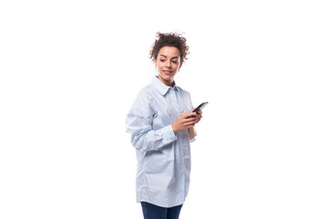 young pretty curly brunette secretary woman oeta in a light blue shirt writes a message on a mobile...