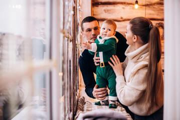 Happy mother, father and baby son sit on windowsill at Christmas time