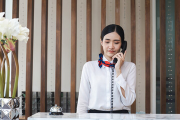 Young Asian woman receptionist behind the hotel counter talking on the phone, Female receptionist...