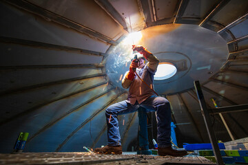 Welding male worker metal arc is part roof tank dome inside confined spaces.