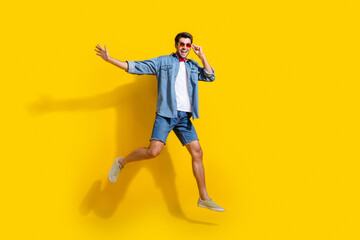 Fototapeta na wymiar Full body photo of satisfied pleasant man dressed denim shirt shorts flying touching sunglass isolated on bright yellow color background