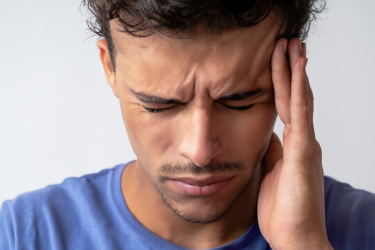 headache. a man in a blue T-shirt stands with a headache and holds his head with his hand