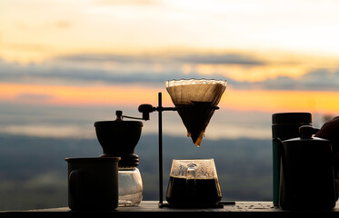 Silhouette, close up of drip coffee set on wooden table with mountain on sunrise background.