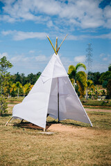 Amidst a lush field a summer wedding tipi offers a charming view. The traditional wigwam adorned with dreamcatcher decorations symbolizes joy and celebration in a natural garden setting. © sorapop