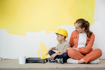 Home repairs. Mom helping her son paint the wall with a roller. The boy paints the wall of the...