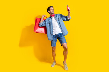 Full body photo of cool man dressed denim shirt shorts holding new outfit in bags look at...