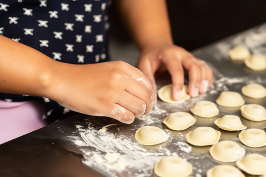 girl with dumplings. a girl stands at a dark table and prepares dumplings, flour is scattered on the table and ready-made dumplings lie