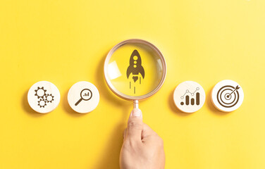 Startup concept. Hand holding magnifying glass focus rocket icon for business goals management and...