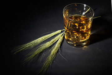 Glass of whiskey with ice and ears of wheat on a black stone table. Top view with copy space