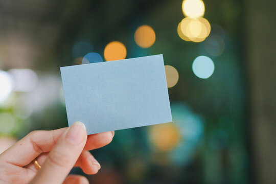 Woman's Hand Holding A Small Blank Blue Paper With Bokeh Background.