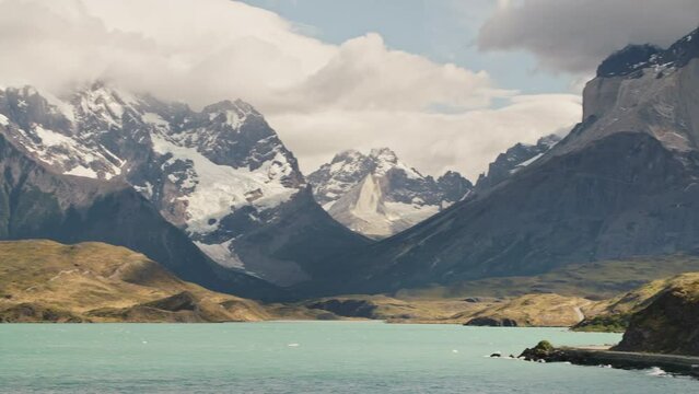 Wide pan over a lake and Los Cuernos in Torres Del Paine nationalpark, Patagonia, Chile to an old VW bus driving along the road.