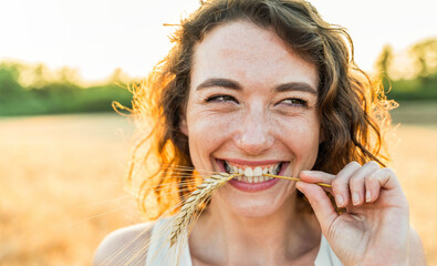 Happy beautiful woman smiling in a wheat field - Delightful female enjoying summertime sunny day...