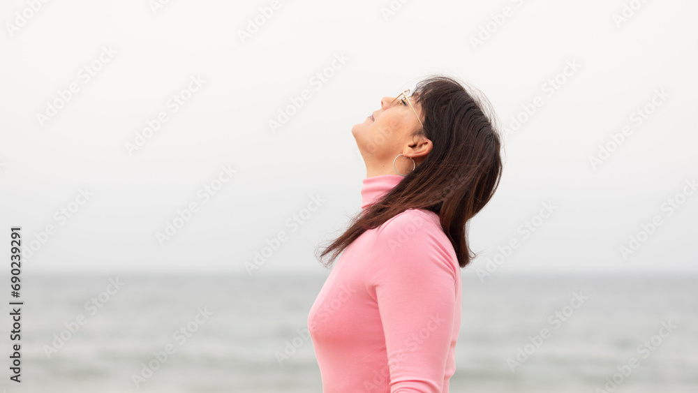 Wall mural the woman is breathing deeply fresh air on the cold winter day with her eyes closed with the sea in 