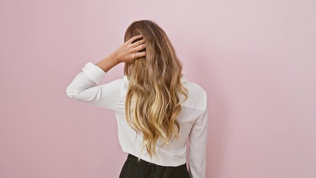 Pensive young blonde woman, hand on head, caught in doubt. beautiful caucasian with backside view, wearing shirt and standing backwards, isolated over pink background wall.