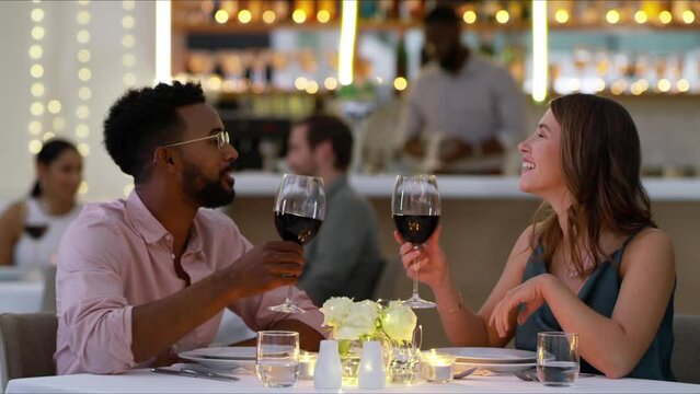Couple in restaurant with wine, conversation and toast at table, valentines day or interracial romance. Fine dining, drinks and cheers, happy man and woman relax on luxury dinner date with smile.